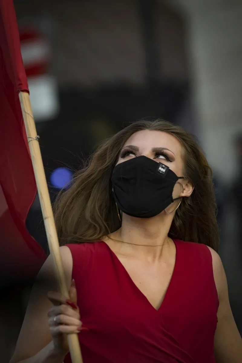 Woman in a red dress and black mask holding a flagpole